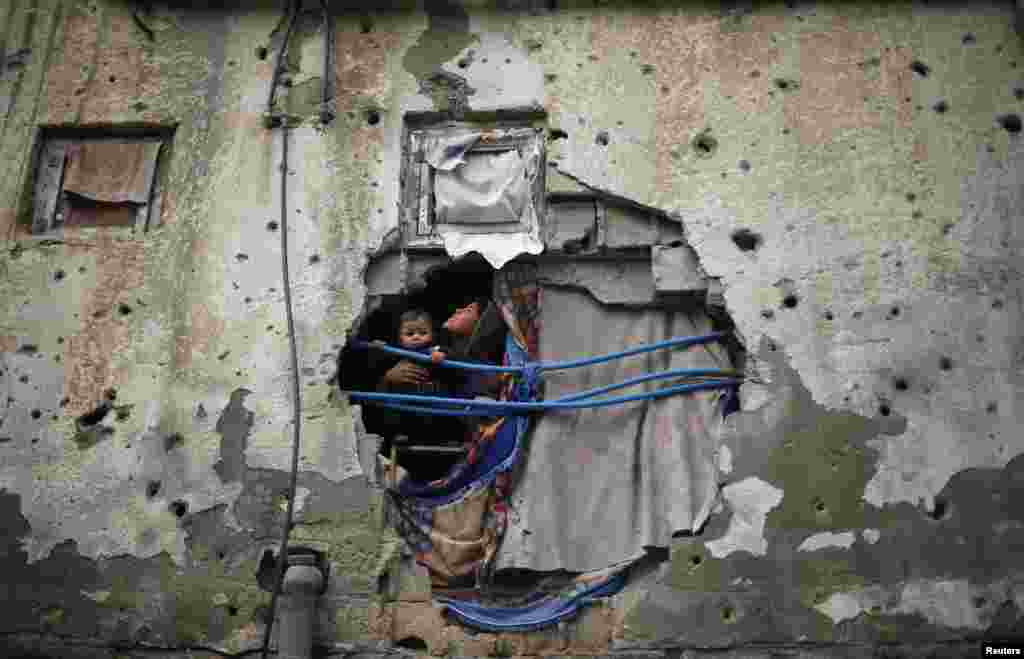 Anak-anak Palestina melongok dari sebuah lobang dinding rumahnya, akibat serangan artileri Israel Juli lalu, yang ditutup dengan selimut di kota Gaza.