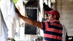 ARCHIVO - Kevin Contreras cuelga toallas y vendas en un granero en Louisville, Kentucky, el martes 18 de abril de 2017. Contreras, un trabajador inmigrante en EEUU con una visa H-2B es uno de los trabajadores de los que depende la industria de las carreras de caballos.