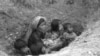 A Cambodian woman with five children apprehensively looks upwards from the shallow bunker as shells from the insurgent forces start falling in the area in the encircled capital of Phnom Penh, in March 1975.