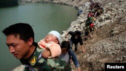 A survivor carries baby on his back as he and some 1,000 other survivors make a nine-hour walk from the village of Qingping to Hanwang, after earthquake, Sichuan Province, China, May 16, 2008.