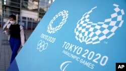 A woman walks near a sing of the Tokyo 2020 Olympic and Paralympic Games, Friday, Aug. 20, 2021, in Tokyo. The Tokyo Paralympics open on Aug. 24 in a ceremony at Tokyo's National Stadium. (AP Photo/Eugene Hoshiko)
