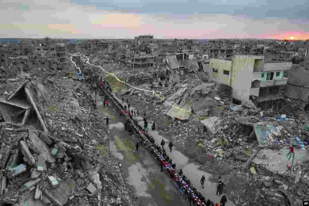 Warga Palestina duduk di meja besar yang dikelilingi puing-puing rumah dan bangunan yang hancur saat mereka berkumpul untuk berbuka puasa, pada hari pertama Ramadan di Rafah, Jalur Gaza selatan. (AP) 