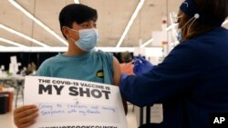 Lucas Kittikamron-Mora (13), memegang tanda untuk mendukung vaksinasi COVID-19 saat disuntik vaksin Pfizer pertamanya di Departemen Kesehatan Masyarakat Cook County, di Des Plaines, Illinois, 13 Mei 2021. 