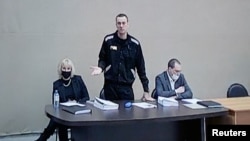El disidente rusos Alexei Navalny (de pie) y sus abogados son vistos en una pantalla a través de un enlace de video durante una audiencia judicial en el centro correccional masculino IK-2, en la ciudad de Pokrov en la región de Vladimir, Rusia, el 15 de febrero de 2022.