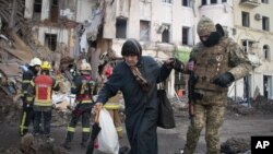 Un voluntario de las Fuerzas de Defensa Territorial de Ucrania ayuda a una mujer a cruzar la calle en Kharkiv, Ucrania, el miércoles 16 de marzo de 2022.