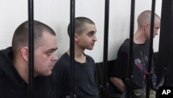 Dos ciudadanos británicos, Aiden Aslin (izq.) y Shaun Pinner (der.), y el marroquí Saaudun Brahim, (centro), tras las rejas en un tribunal en Donetsk, bajo el control del autoproclamado Gobierno de la República Popular de Donetsk, en el este de Ucrania, el 9 de junio de 2022.