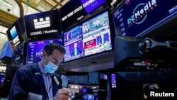 Seorang pialang saham tampak sibuk bekerja di saat layar di belakangnya menampilkan pidato dari Kepala Bank Sentral AS Jerome Powell, di Kantor Bursa Saham New York, pada 26 Januari 2022. (Foto: Reuters/Brendan McDermid)