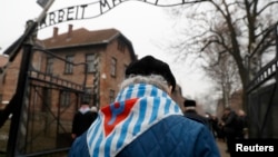 Para penyintas dan tamu berjalan melewati gerbang bekas kamp konsentrasi dan pemusnahan Nazi bertuliskan"Arbeit Macht Frei" ("Bekerja Membebaskan Anda") Auschwitz, dalam acara peringatan 73 tahun pembebasan kamp dan korban Holocaust, di Oswiecim, Polandia, 27 Januari 2018.