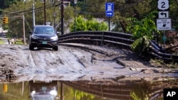 ARCHIVO - Un conductor se detiene en un puente cubierto de lodo mientras decide si atravesar una zona inundada en el río Winooski, el 12 de julio de 2023 en Montpelier, Vermont. 