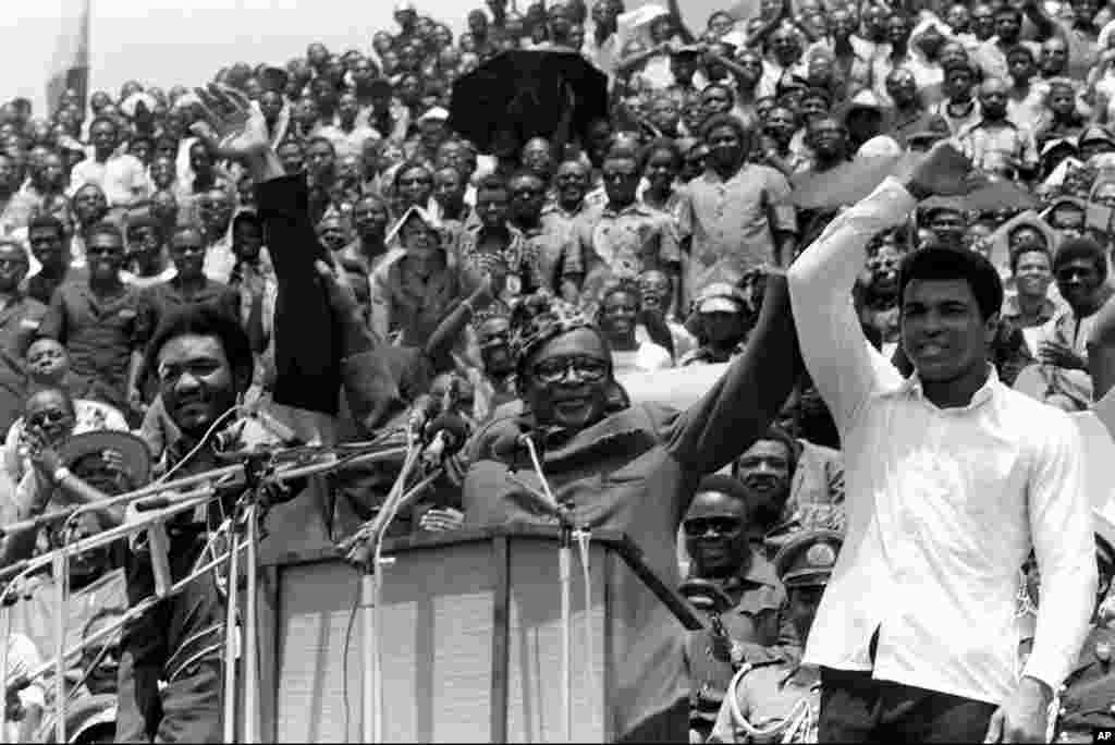 Le président du Zaïre Mobutu Sese Seko, lève la main de Muhammad Ali quand il le présente avec son challenger George Foreman avant le combat du championnat WBA/WBC au cours d’un meeting populaire au stade du 20 Mai où les deux boxeurs disputeront le titre quelques jours plus tard. (AP Photo).