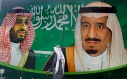 FILE - A man walks past a banner showing Saudi King Salman, right, and his Crown Prince Mohammed bin Salman, outside a mall in Jiddah, Saudi Arabia, March 7, 2020.