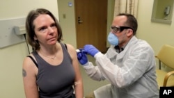 A pharmacist gives Jennifer Haller, left, the first shot in the first-stage safety study clinical trial of a potential vaccine for COVID-19, the disease caused by the new coronavirus, Monday, March 16, 2020 at the Kaiser Permanente Washington Health Research Institute in Seattle.