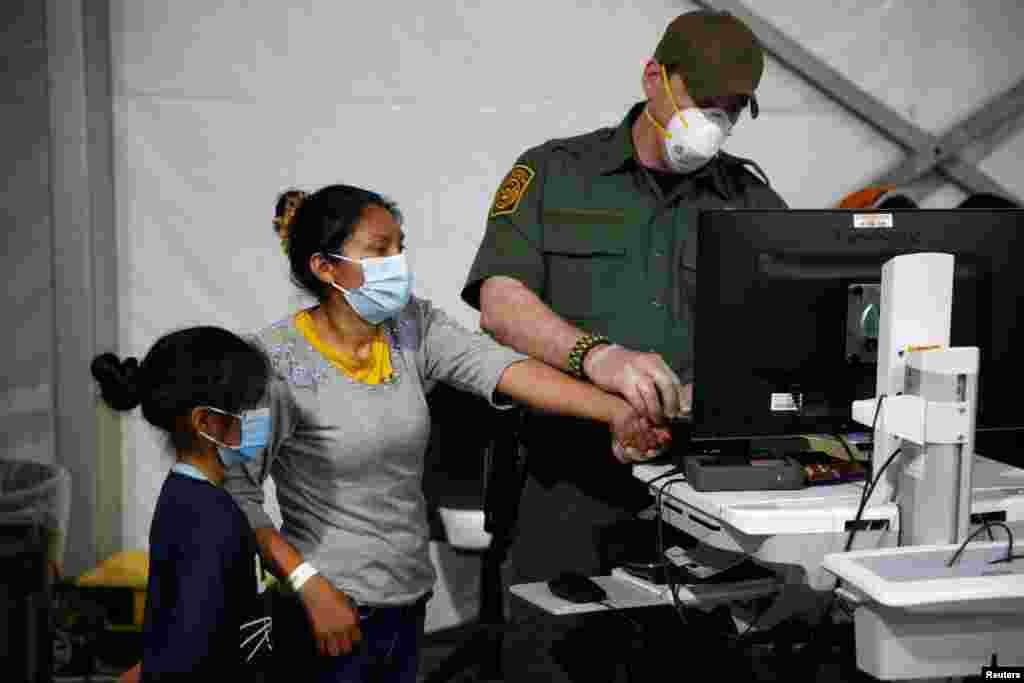 Un oficial toma los datos biométricos de una migrante y su hija que ingresan en el área de admisión del centro de detención.