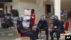 Zambian police sit at the Civic Center in Lusaka as election volunteers carry ballot boxes, Sept. 22, 2011.
