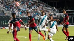 El mediocampista guatemalteco Carlos Mejía (6) dispara al arco ante el defensa cubano Dariel Morejón (5) y el mediocampista Neisser Sandó (14) durante la primera mitad de un partido de fútbol de la Copa Oro de CONCACAF, el martes 27 de junio de 2023, en Fort Lauderdale, Florida.