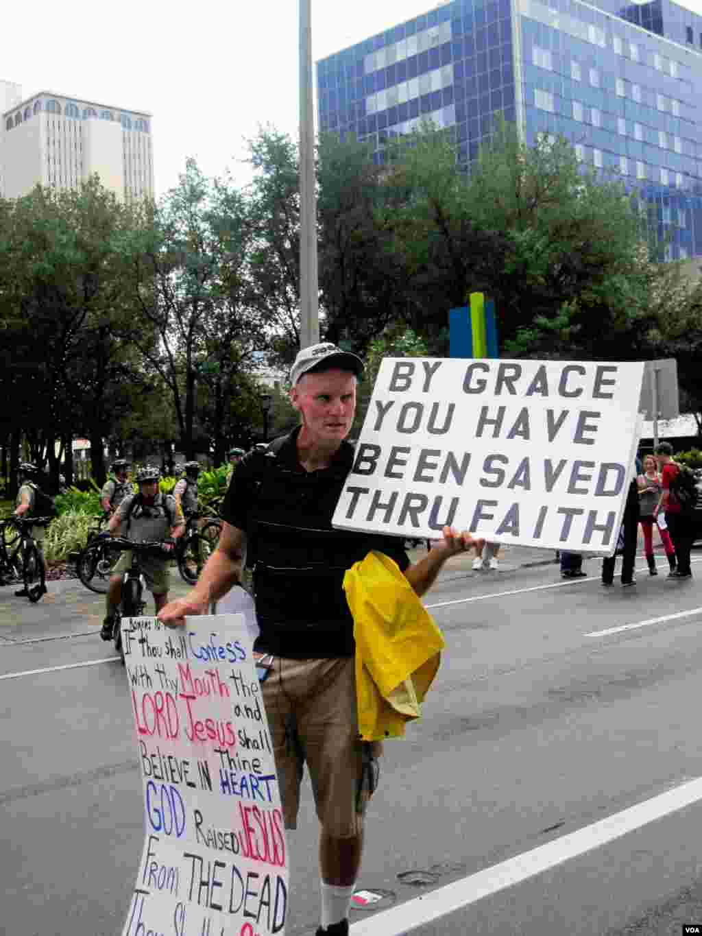 Seorang pria dari kelompok Occupy Tampa menggelar papan-papan bertuliskan berbagai slogan dalam aksi protes di dekat arena Konvensi Nasional Partai Republik, Tampa, Florida, Senin (Eva Mazrieva/VOA).