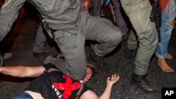An Israeli police officer puts his knee on a demonstrator to make an arrest during a protest against Israeli Prime Minister Benjamin Netanyahu outside his residence in Jerusalem, July 22, 2020.