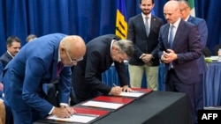 Los delegados jefe del gobierno de Nicolás Maduro y la oposición venezolana, Jorge Rodríguez y Gerardo Blyde, firman los Acuerdos de Barbados bajo la mirada del diplomático noruego Dag Nylander, a la derecha, el 17 de octubre de 2023, en Barbados.