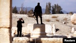 A Syrian army soldier takes a picture of a fellow soldier standing on ruins in the historic city of Palmyra, Syria, March 4, 2017.