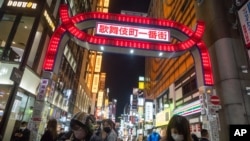 People walk by a street filled with entertainment, restaurants and bars in the Shinjuku neighborhood of Tokyo on Friday, April 9, 2021. Japan announced Friday that it will raise the coronavirus alert level in Tokyo to allow tougher measures to curb…