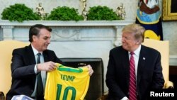 El presidente de Brasil, Jair Bolsonaro, regala a su homólogo estadounidense, Donald Trump, una camiseta de la 'canarinha' con su nombre a la espalda durante el encuentro que ambos mandatarios mantuvieron en la Casa Blanca el 19 de marzo de 2019.