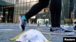 2020年3月14日，一名女子从特朗普大厦附近街面上一个用过的防护口罩旁走过。