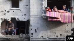 Niños juegan en el balcón de un apartamento junto a un hombre que revisa la destrucción después de un ataque israelí en el campamento de Nuseirat, Gaza, el 10 de diciembre de 2024.