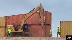 ARCHIVO - Esta fotografía proporcionada por la oficina del gobernador de Arizona muestra a varios trabajadores moviendo contenedores de carga el 12 de agosto de 2022.