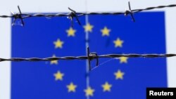 A barbed wire is seen in front of a European Union flag at an immigration reception center in Bicske, Hungary, June 25, 2015. 
