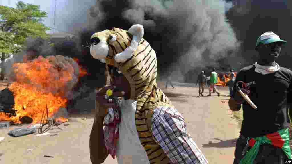 Les manifestants se tiennent devant le parlement où des voitures et des documents brulent, à Ouagadougou le 30 Octobre, 2014. Des centaines de manifestants en colère au Burkina Faso ont pris d'assaut le parlement le 30 Octobre avant d'y mettre le feu en signe de protestation contre l'intention de modifier la Constitution pour permettre au Président Blaise Compaoré pour étendre son règne de 27 ans. AFP PHOTO / ISSOUF SANOGO