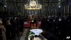 Seorang wanita mencium layar pelindung di atas peti mati Patriark Irinej saat dia berbaring di gereja Kongregasional di Beograd, Serbia, Sabtu, 21 November 2020. (Foto: AP)