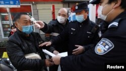 湖北武漢街頭設立的檢查卡社區工作人員檢測行人的體溫，警察檢查其身份文件。 （2020年2月20日）