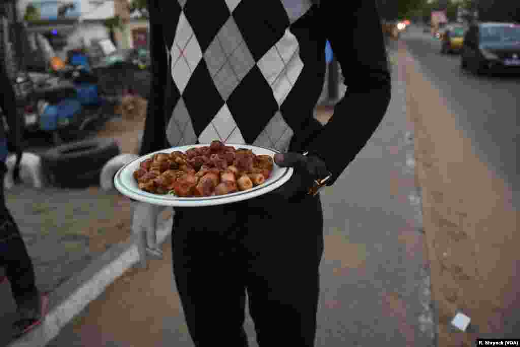 A man hands out dates to taxi drivers and bus passengers along a busy street in Dakar, Senegal, May, 23, 2018, as the sun sets. Devout Muslims break the fast in Senegal as they prepare large quantities of food and drink to share with those around them. 