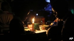 FILE - With electricity unavailable or unaffordable for many, Learnmore Mavhura, right, helps his 9-year old nephew, Lionel, do his homework by candlelight, in Harare, Zimbabwe, July 23, 2019.