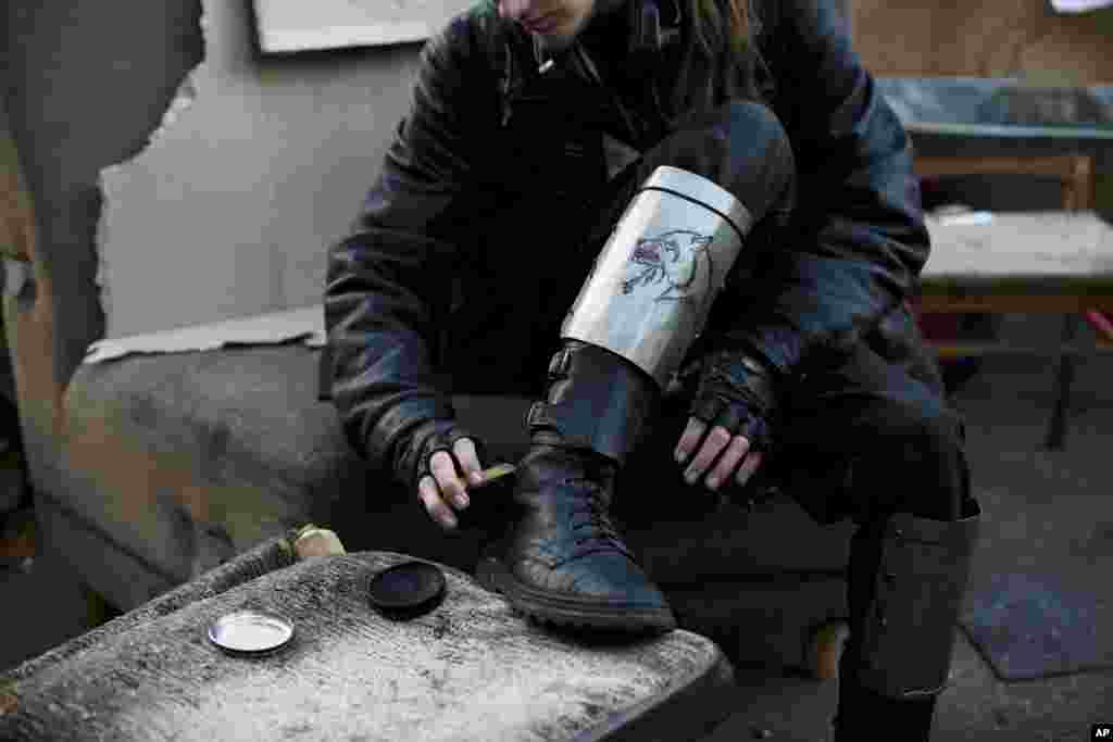 A member of a self-defense volunteer group, with makeshift shin guards bearing a picture of a wolf, polishes his boots in Kyiv's Independence Square, March 11, 2014. 