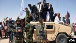 Des militants talibans afghans se tiennent debout sur un véhicule blindé de l'Armée nationale afghane (ANA) alors qu'ils célèbrent un cessez-le-feu le troisième jour de l'Aïd dans le district de Maiwand dans la province de Kandahar le 17 juin 2018.