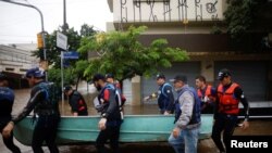 Los remeros preolímpicos brasileños Evaldo Mathias Becker y Piedro Tuchtenhagen y otros llevan un barco utilizado para rescatar a las víctimas de las inundaciones en Porto Alegre, estado de Rio Grande do Sul, Brasil, 10 de mayo de 2024.