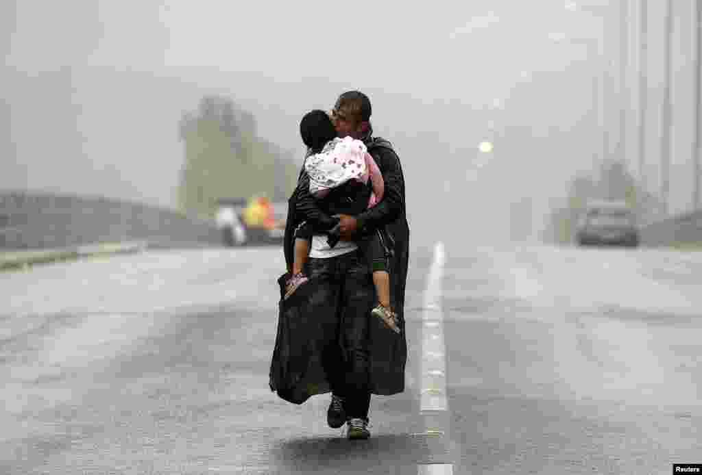 A Syrian refugee kisses his son as he walks through a rainstorm towards Greece's border with Macedonia, near the Greek village of Idomeni.