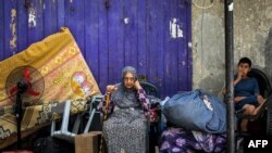 Seorang perempuan dan anak menunggu dengan barang-barangnya sebelum dievakuasi dari Rafah di Jalur Gaza selatan pada 11 Mei 2024, di tengah konflik di wilayah Palestina antara Israel dan Hamas. (Foto: AFP)