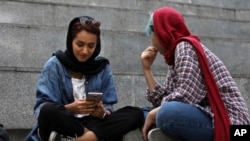 FILE - A woman checks her cell phone sitting with a companion on the steps outside a shopping mall in northern Tehran, Iran, July 2, 2019.