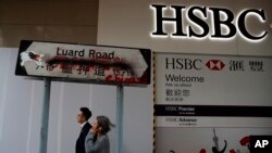 People walk by a vandalized road sign near a HSBC Bank branch covered by panels after damaged by pro-democracy protesters in Hong Kong, Jan. 4, 2020.