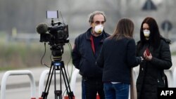 Reporteros usando mascarillas trabajan en la entrada del pequeño pueblo de Casalpusterlengo, en el sudeste de la península italiana, luego que el gobierno impusiera drásticas medidas de contención del brote.