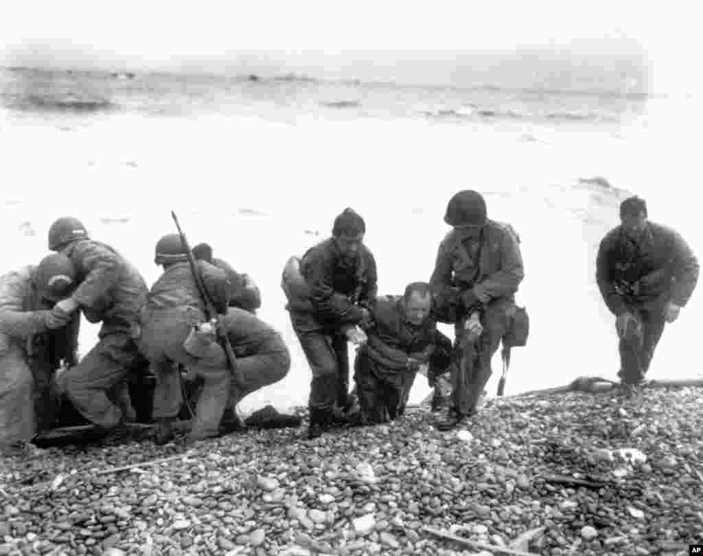 Members of an American unit reach Utah Beach on a life raft after their landing craft was hit and sunk by German coastal defenses. Here soldiers help their exhausted comrades ashore during the Normandy invasion, June 6, 1944. 
