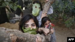 Des enfants palestiniens posent avec des masques de fortune faits avec des feuilles de chou lorsqu'ils cuisinent à la maison avec leur famille à Beit Lahia dans le nord de la bande de Gaza le 16 avril 2020. (Photo: MOHAMMED ABED / AFP)