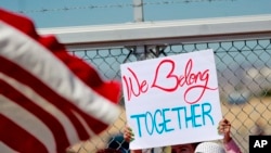 A protester holds a sign outside a closed gate at the Port of Entry facility, June 21, 2018, in Fabens, Texas, where tent shelters are being used to house separated family members.