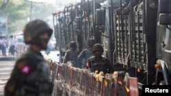 FILE - Soldiers stand next to military vehicles as people gather to protest against the military coup, in Yangon, Myanmar, Feb. 15, 2021. Myanmar's military junta is ordering a mandatory draft set to begin in mid-April 2024.