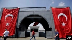 Men walk at the Galata bridge past two Turkey flags, in Istanbul, on Tuesday, Aug. 2, 2016. 