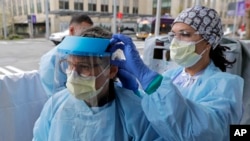 Tilliesa Banks, right, an emergency services nurse at Harborview Medical Center in Seattle, helps a colleague put on a medical face shield prior to their shift in a triage tent outside the Harborview emergency department.