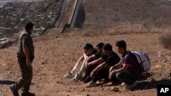 El agente de la Patrulla Fronteriza Gutiérrez pasa junto a cuatro hombres detenidos después de cruzar la frontera ilegalmente en un espacio en dos muros que separan a México de Estados Unidos antes de entregarse, el jueves 23 de enero de 2025, en San Diego. AP