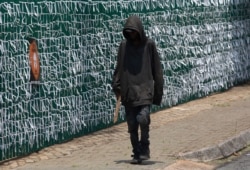 A pedestrian passes the perimeter fence of the Presbyterian Church in Bedfordview, Johannesburg South Africa, Wednesday, Jan. 20, 2021. The fence is covered with ribbons to represent a person who has died in the COVID-19 pandemic. (AP Photo/Denis…